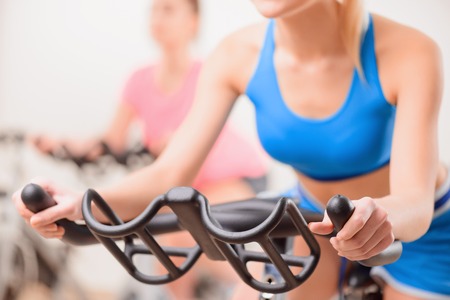 Cycling on exercise bikes. Cropped image of two attractive young women in sports clothing exercising...