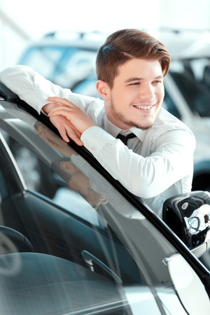 I love my job. Closeup of handsome young car salesman in formal wear standing at the dealership and...