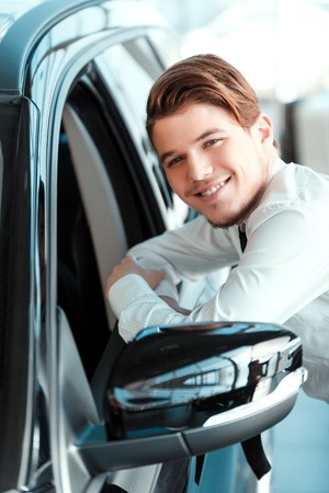 I love my job. Closeup of handsome young car salesman in formal wear standing at the dealership and...