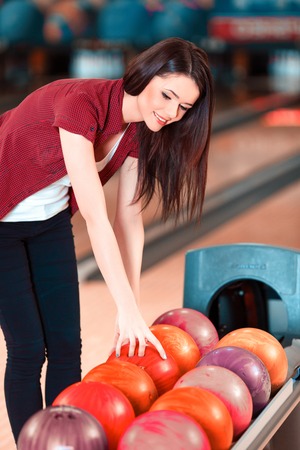 Choosing a ball. Cheerful young women choosing bowling ball and smiling while standing against bowling alleysの写真素材
