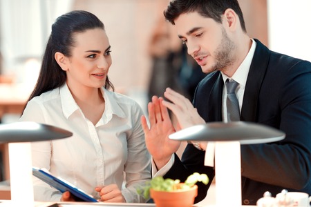 Closeup of handsome young man and woman looking at documents with marketing data while sitting at the restaurantの写真素材