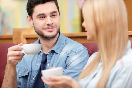Enjoying fresh coffee together. Closeup of beautiful young couple looking at each other and smiling while enjoying coffee in cafe togetherの写真素材