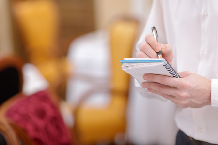 Taking the order. Cropped image of handsome young waiter in shirt and bow tie holding a notepad and taking an order in the luxury restaurantの写真素材