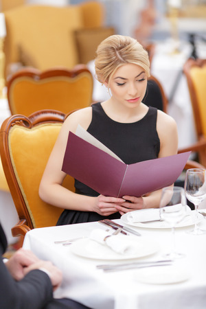 She knows what she wants. Beautiful young woman looking at the menu and smiling while sitting at the restaurantの写真素材