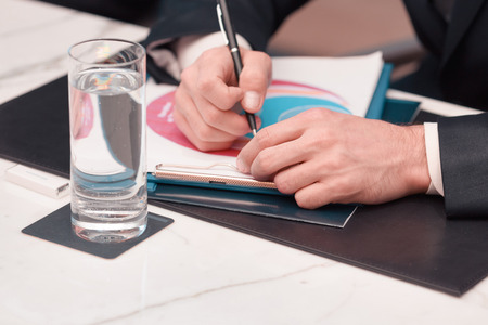 Businessman on business meeting. Cropped image of business man in formalwear holding a pen while sitting at the table with a glass of waterの写真素材