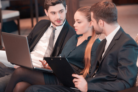 Business team brainstorming. Group of business people in formal wear sitting together on the couch and discussing something while looking at the laptopの写真素材