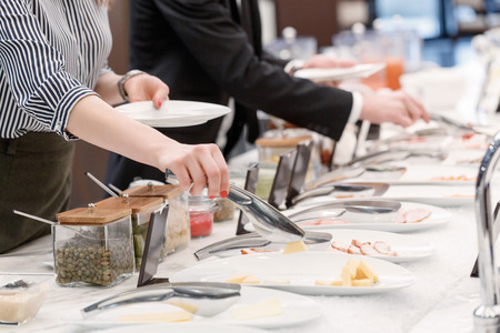 Tasty cheese and meat appetizers at the buffet table. Cropped close up of a female hand taking...