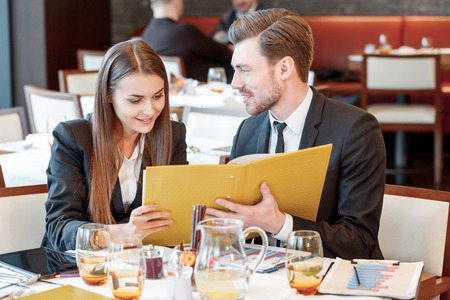Passionate about business. Young smiling business manager smiles to his female colleague while they look through the business papers during the lunchの写真素材
