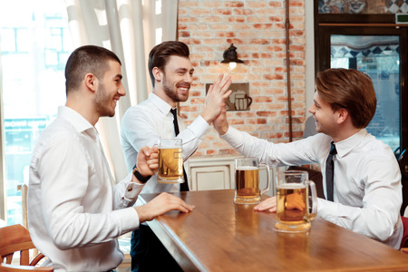 Celebrating success together. Two cheerful young men in shirt and tie gesturing while drinking beer at the bar counterの写真素材