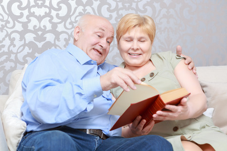 Enjoyable leisure. Cute senior couple looking through the book sitting on the couch at homeの写真素材