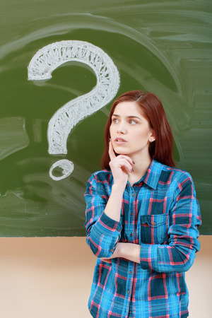 Mystery. Young thoughtful student thinking on some question with a question mark on a chalkboard on the backgroundの写真素材