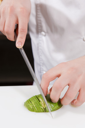 Cooking craft. Close-up on hands of a cook skillfully slicing an avocadoの写真素材