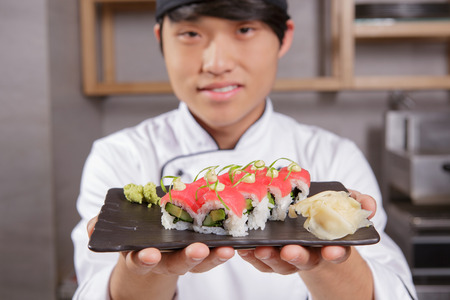 Here is your meal. Closeup of a rectangular plate with tuna sushi with avocado, hazel sauce and seaweed served with wasabi and ginger in focusの写真素材