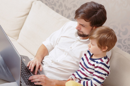 Digital age. Top view of a young handsome man and his son using computer in a living roomの写真素材
