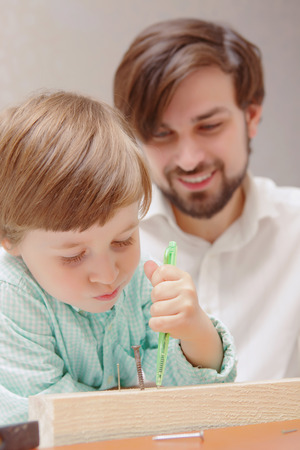 Being precise. Close-up of a smiling father and serious little son putting marks with a pen in toy constructorの写真素材
