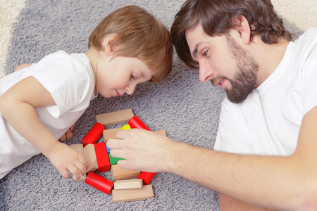 Family interaction. Young handsome father and cute son play building kit lying on a carpet in children roomの写真素材