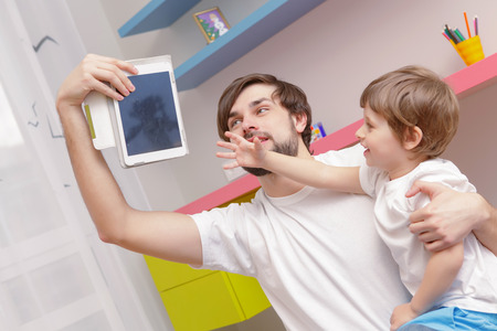 No cartoons. Young father taking away a tablet device from his small son who stretches out his hand to grab itの写真素材
