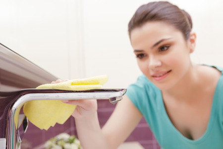 Highly polished. Smiling woman wiping shiny tap in bathroom with help of yellow clothの写真素材
