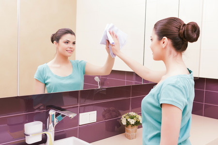 Pedantic. Young woman carefully wiping tap in bathroom with help of yellow clothの写真素材