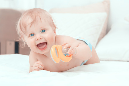 Childhood. Portrait of a small baby boy lying on the bed smiling and holding his toyの写真素材
