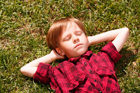 Sweet dreams. Little boy lying on grass with hands behind his head and sleeping.の写真素材
