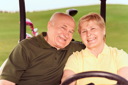 To next hole. Portrait of senior man and woman driving in cart on course.の写真素材