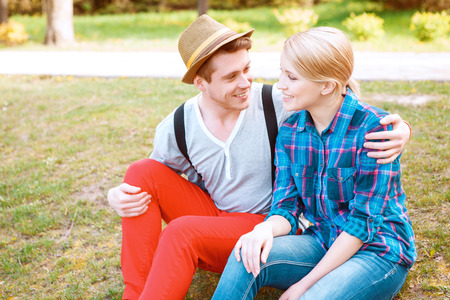 Soft glance. Sweet lovely couple sitting on grass in park and embracing each other.の写真素材