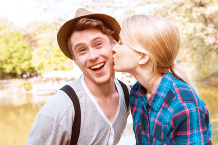 So happy. Beautiful young lady giving kiss to cheek to his boyfriend in park on background of lake.の写真素材