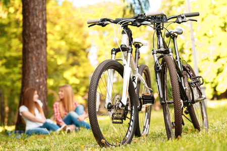 Selective focus on two sport bikes standing near while young beautiful girls with long hair sitting on a blue checkered mat under a tree, smiling happily on the backgroundの写真素材