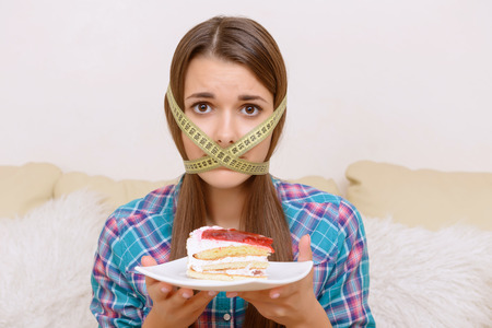 Strict diet.  Girl having centimeter band on her head and cake in arms.の写真素材