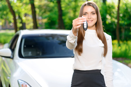 Here it is. Pretty young woman standing in front of car and showing key.の写真素材