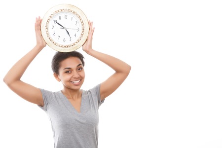 Feeling funny. Funny young mulatto girl holding big clock above her head on white isolated backgroundの写真素材