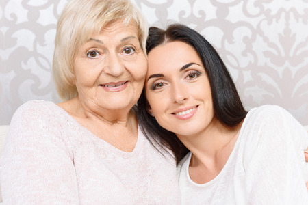Pretty women. Two smiling pleasant women of different ages leaning on each other.の写真素材