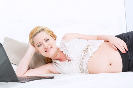 Cheerful mind. Pregnant young woman touching her belly and smiling while having rest on the couch.