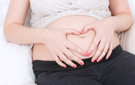 Love in motion. Pregnant young woman keeping her hands on belly and relaxing on the couch.