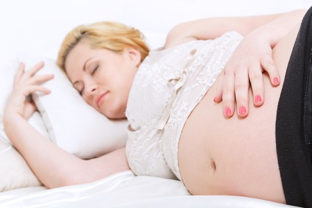 Sweet dreams. Pregnant young woman touching her belly while having a nap on bed.の写真素材