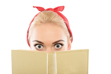 Portrait of a beautiful blond pin up girl with ponytail and red bandana hiding behind a yellow book...