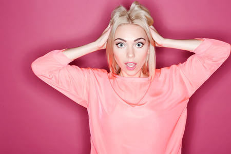 Oh my god. Portrait of young pretty woman touching her hair with great amazement on isolated pink backgroundの写真素材