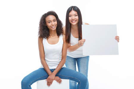 Look attentive. Upbeat smiling girl keeping white card in her hands and leaning ahead with another girl sitting beside.の写真素材