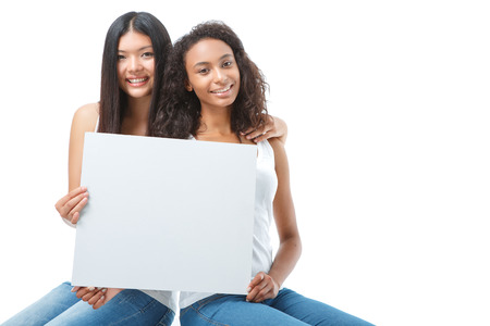 Longlasting friendship. Pair of young ladies sitting on the box and holding white card while bonding to each other.の写真素材