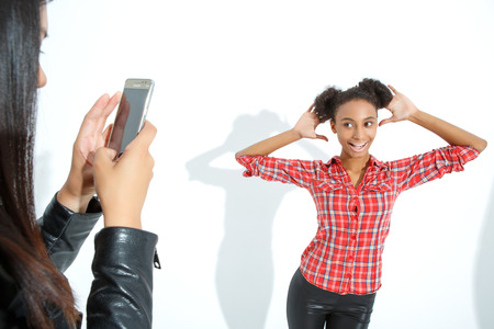 Looking funny. Pretty young girl holding her hands near her face and smiling while the friend making shotsの写真素材