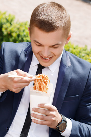So tasty. Youthful businessman eating Chinese noodle soup outside with great enthusiasmの写真素材