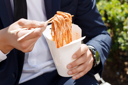 Fast food. Close up of businessman holding package with Chinese noodles.の写真素材