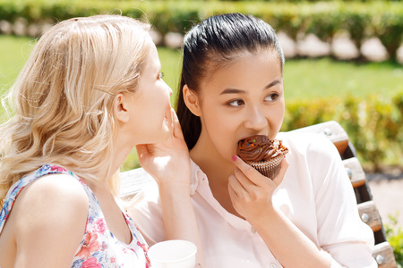 Telling secrets.  Young blond-haired girl telling secret to her friend with cupcake.の写真素材
