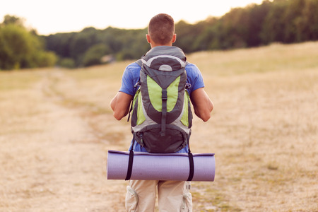 Back view of a young tourist wearing blue t-short and beige shorts with a big traveling backpack...