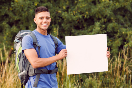 Traveling. Portrait of a young handsome tourist wearing blue t-short and backpack standing looking at the camera smiling and holding copy spaceの写真素材