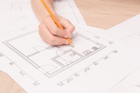 Real engineer. Close up of young husband holding pencil and making drawings of his new flat on the floorの写真素材