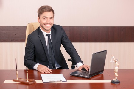 Love my job. Upbeat handsome man sitting at the table and smiling while being busy at work
