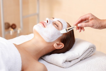 Find peace in mind. Spa specialist holding brush and making mask to lovely woman lying in spa salonの写真素材