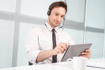 Busy at work. Positive handsome call center operator sitting at the table and holding laptop while...